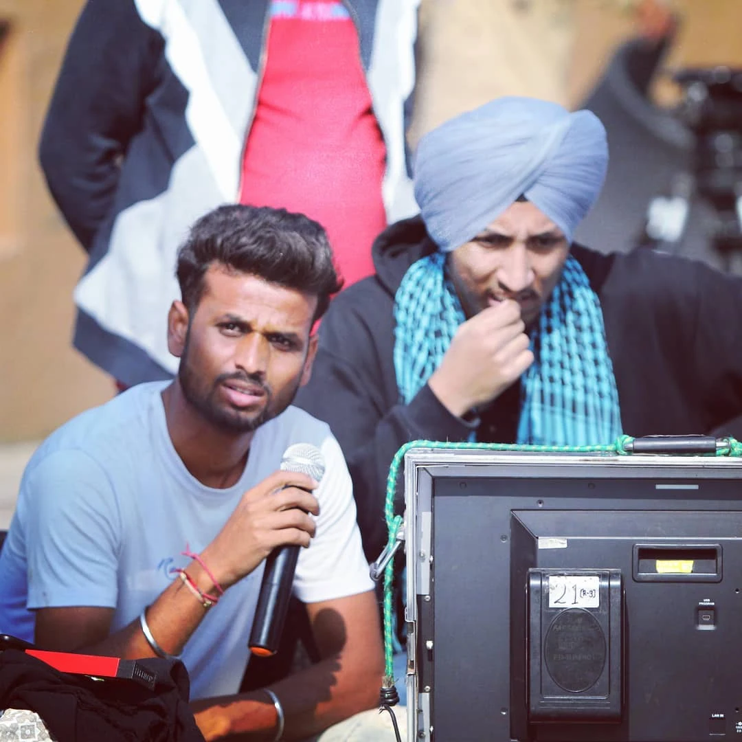 Suraj Kumar on set, holding a microphone beside a production monitor